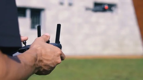 A man controls a drone near a gray building on a green lawn. Summer. Close-up Stock Footage 80686778