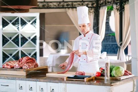 A man cook cuts meat with a knife in a restaurant. Stock Photos