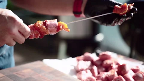 Man in cooking gloves stringing pieces of spicy sausages and marinated beef meat Video stock 132694345