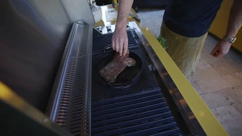 A man is cooking on a grill with a pan on top of it Stock Footage 297871765