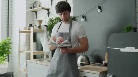 Man cooking in kitchen reading recipe from cookery book. Stock Footage 150029340