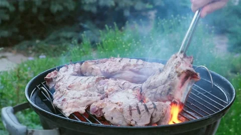 Man cooking meat on black round barbecue rotating beaf steaks open fire smoke Stock Footage 130667191