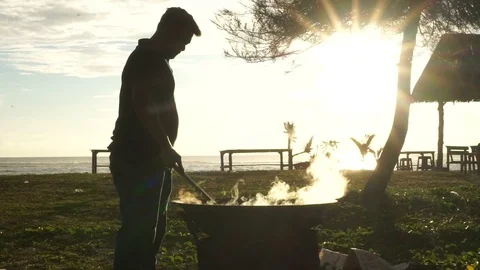 Man cooks in beach while sunset comes Stock Footage 113863019