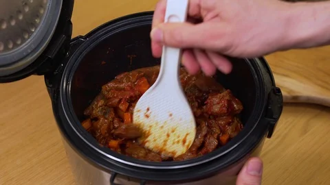 A man cooks the beef in a slow cooker, mixing it with a spoon Stock Footage 129101073