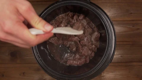 A man cooks beef stew in a slow cooker stir with a spoon Stock Footage 129100978