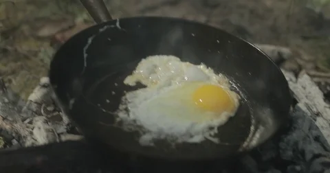 Man cooks egg in frying pan on campfire Stock Footage 76703624