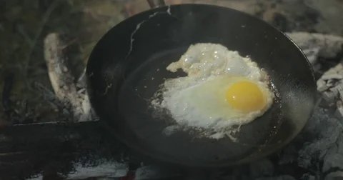 Man cooks egg in frying pan on campfire Stock Footage 76703654