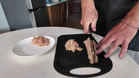 Man cooks in a home kitchen, a close-up of his hands can be seen cutting meat Stock Footage 330059696