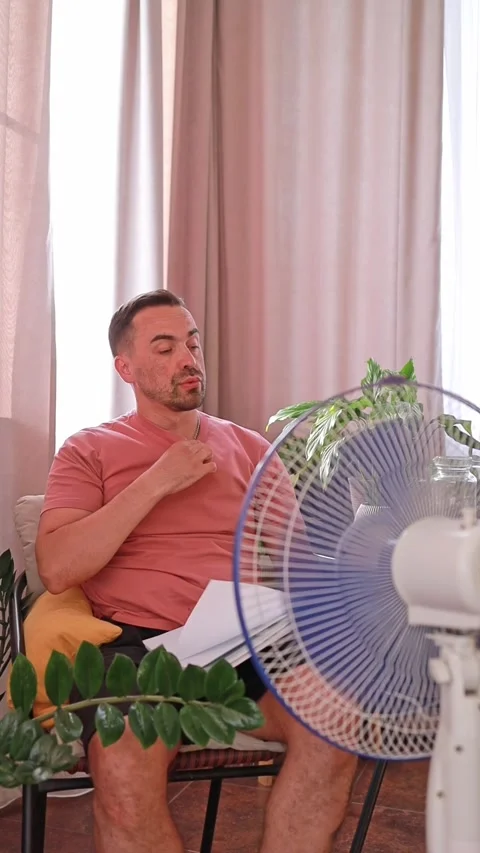 A man cools down under a fan on a hot day, escaping from the stuffiness and heat Stock Footage 310992738