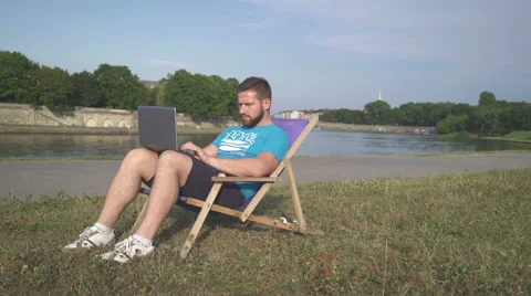 Man is coping data from smartphone to laptop, lying on sunbed. 库存影片 65205498