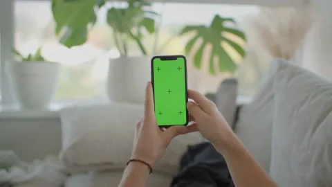 Man on couch lifts iphone into frame, green screen mockup 库存影片 218466952