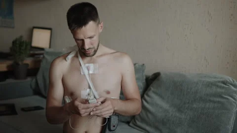 Man on couch presses buttons on portable medical device for ECG monitoring. Stock Footage 249585191