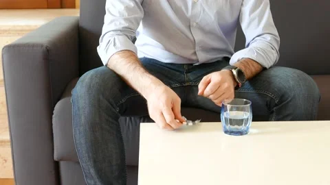 Man on the couch takes a pill and drinks a glass of water Stock Footage 138329077