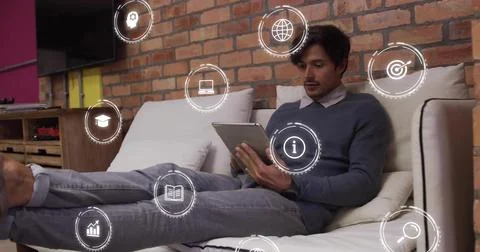 Man on couch tapping tablet, causing icons appearing around him, sitting, Stock Photos