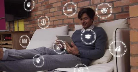 Man on couch tapping tablet, causing icons appearing around him, sitting, Stock Photos