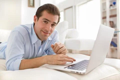Man on couch using laptop, looking camera Stock Photos