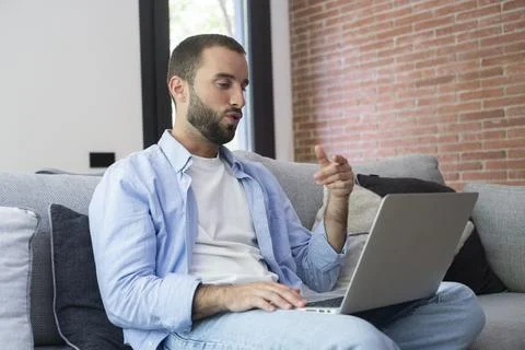 Man on couch using laptop for a video call at home, casual remote work and .. Foto stock