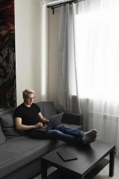 A man on the couch is working at home using a laptop. Remote work concept Stock Photos