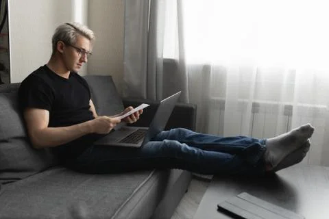 A man on the couch is working at home using a laptop. Remote work concept Stock Photos