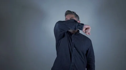 Man coughs forcefully on arm as prevention measure on gray background Stock Footage 129420720