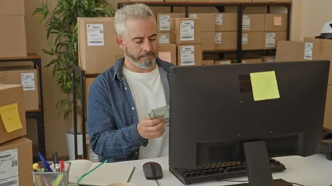 Man counting cash and writing at a computer monitor amid stacked parcel box.. Stock Footage 337437355