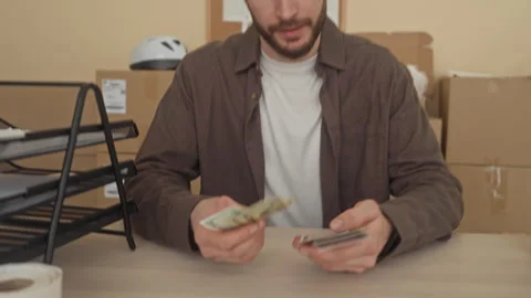 Man counting cash with hands at cluttered desk amid delivery parcels and st.. Stock Footage 337362465