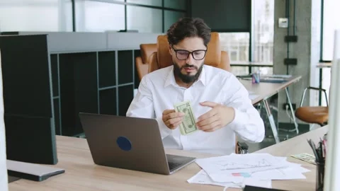 Man counting cash while working at a modern office desk in a bright workspace Stock Footage 315783193