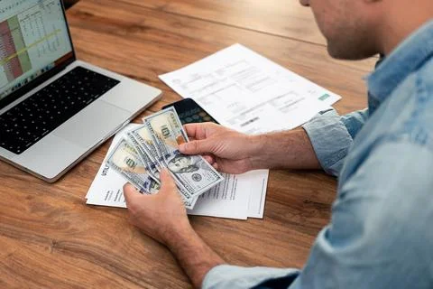 Man counting dollar bills while reviewing utility bills and household expenses Stock-Fotos