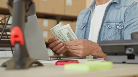 Man counting dollars with hands by laptop and parcels at packing desk in bu.. Stockbeeldmateriaal 337372152
