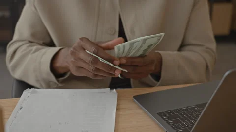 Man counting dollars with hands over laptop and papers at a desk inside a b.. 動画素材 337434741