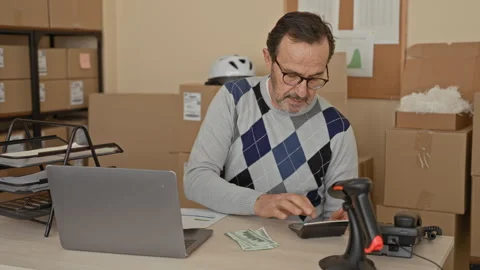 Man counting dollars at laptop among cardboard boxes and parcels in a build.. Stock Footage 337443774