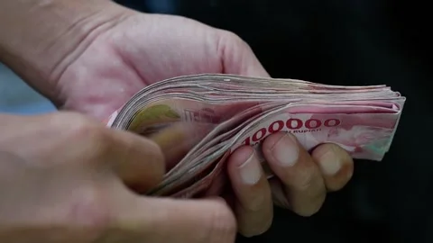 A man counting a pile of hundred thousand rupiah notes Stock Footage 272550198