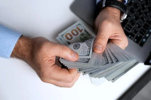 Man counting stack of hundred-dollar bills at desk, close-up Stock Photos