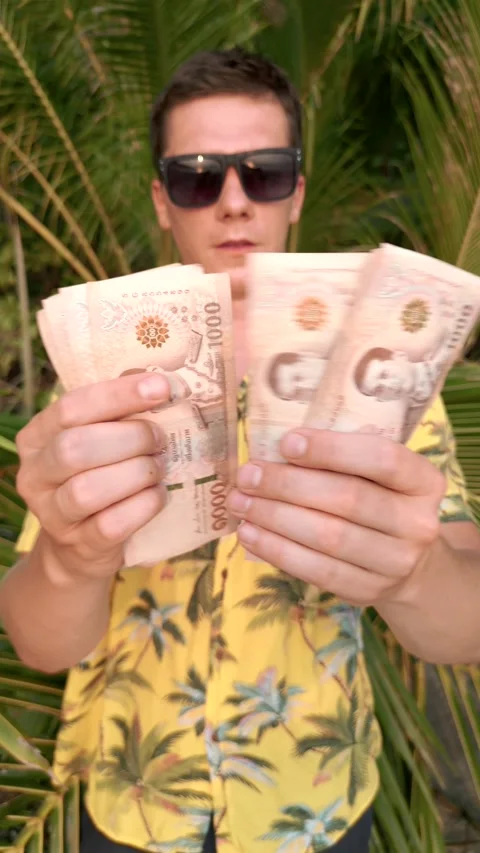 Man counting Thai Baht on a beach with palm leaves in the background Stock Footage 239045685