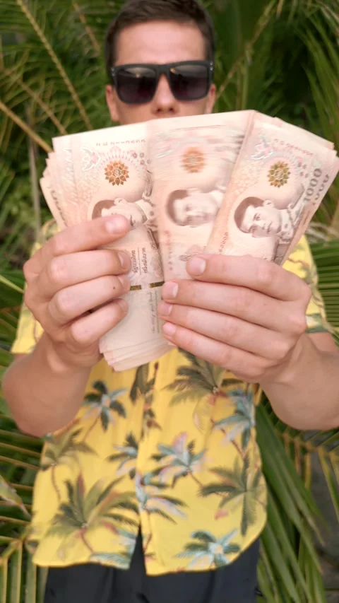 Man counting Thai Baht on a beach with palm leaves in the background Stock Footage 240158209