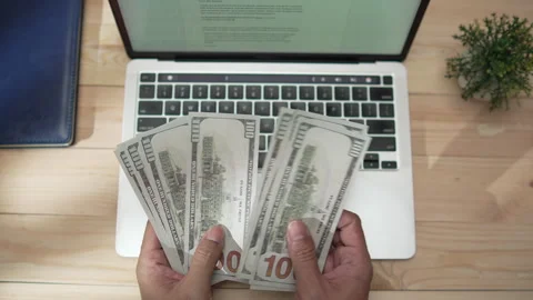 A man counting US dollar bills on top of a laptop, viewed from above Stock-Footage 346770717