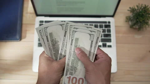 Man counting US dollar bills beside a laptop on a minimalist wooden table Stock-Footage 346770996