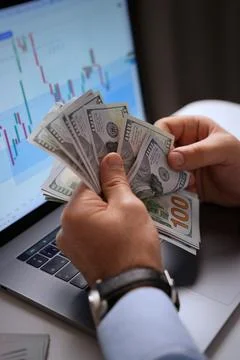 Man Counting US Dollars in Front of Laptop with Trading Chart Stock Photos