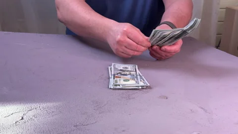 Man counting a wad of dollars sitting at a table side view, close-up on his hand Stock Footage 304754484