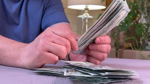 Man counting a wad of dollars sitting at a table side view, close-up on his hand Stockbeeldmateriaal 304755387
