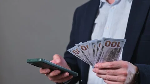 A man counts cash in his hands while holding a mobile phone in the other. He Stock Footage 338300051
