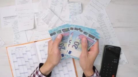 Man counts euro banknotes while managing finances, surrounded by receipts Stock Footage 340920824