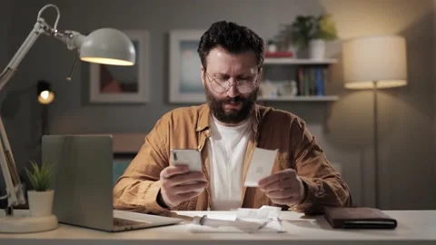 Man counts pay checks. Upset bearded man at home counts expenses on calculator Stock-Footage 188745366