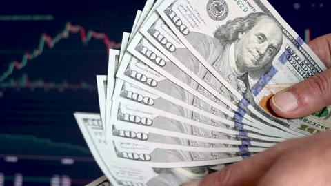 A man counts US dollars in front of a stock market price chart screen Stock Footage 303505162