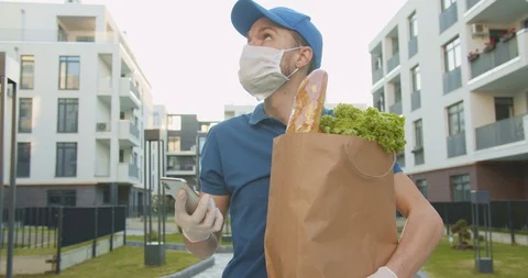 Man courier in blue hat holding food packet and tapping, texting message on Stock Footage 129711264