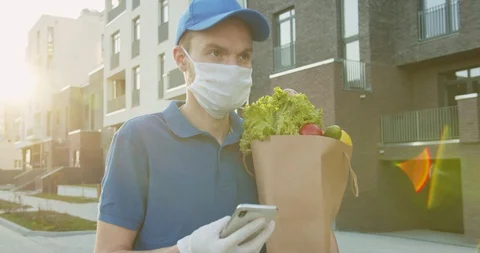 Man courier in blue hat walking street and holding food packet, tapping, texting Stock Footage 129680414