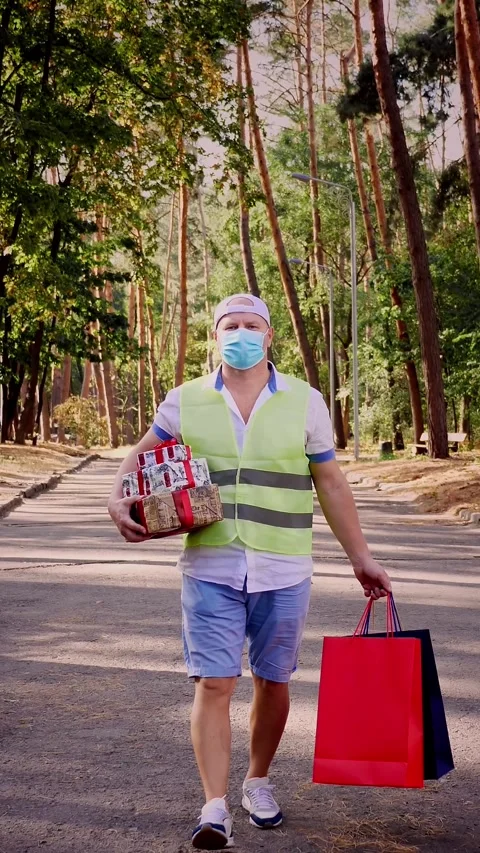 Man, courier, in protective mask, holding several wrapped gift boxes and Stock Footage 317441133