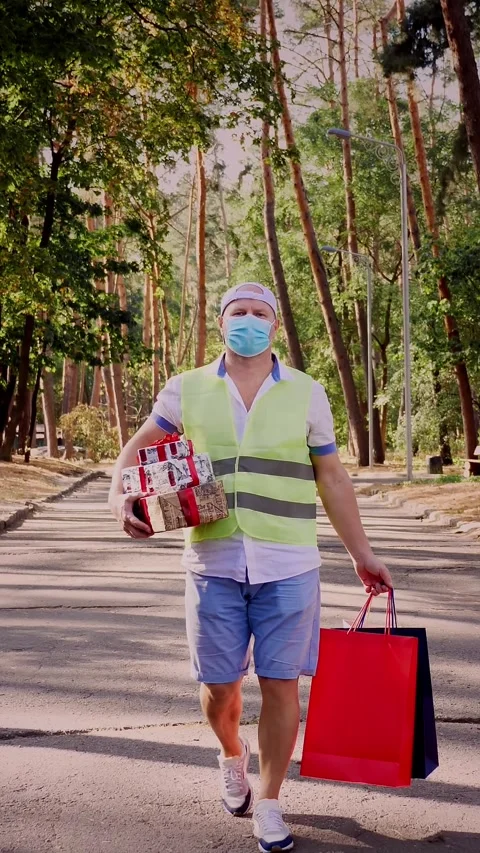 Man, courier, in protective mask, holding several wrapped gift boxes and Stock Footage 317851365