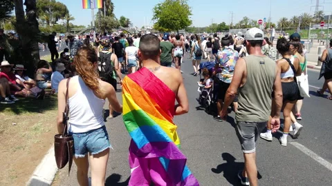 A man covered with a rainbow flag walks among people at the pride parade Stock Footage 197342594