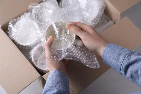 Man covering ceramic dishware with bubble wrap, closeup Foto stock